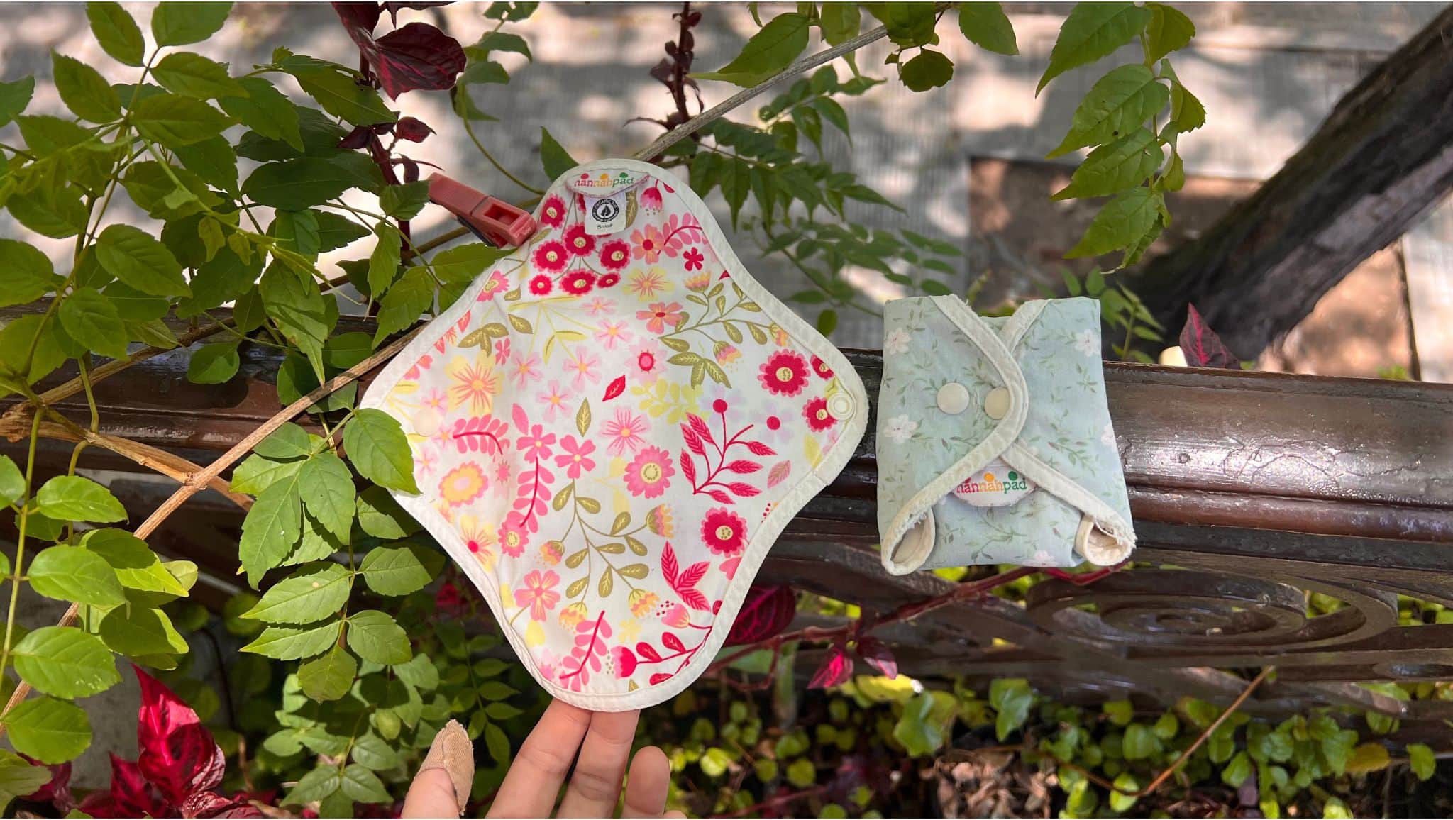 Two colorfully designed reusable pads laying atop green plants.