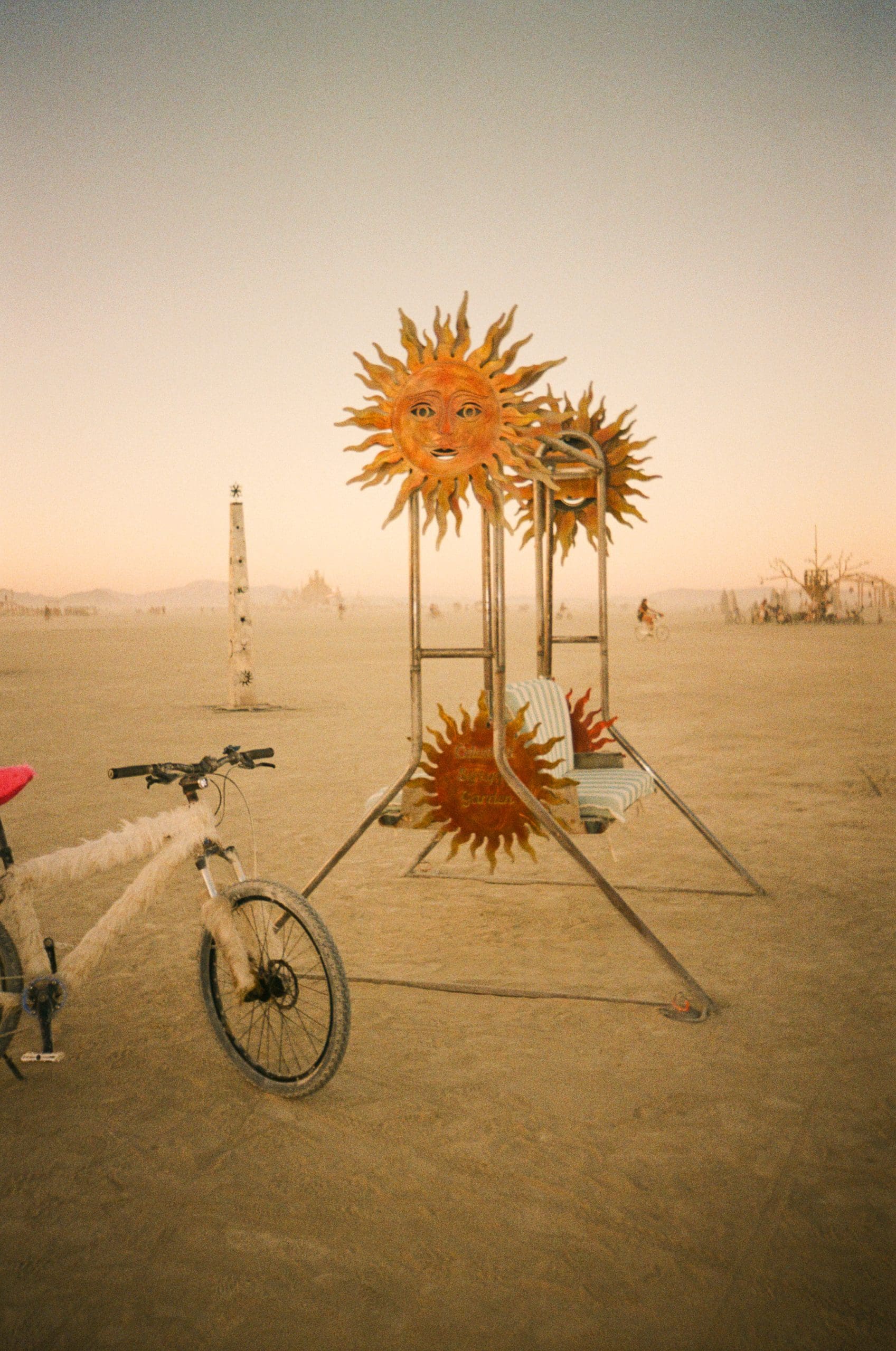 An orange sun art installation with a bike in front taken on 35mm film in the desert of Burning Man. 