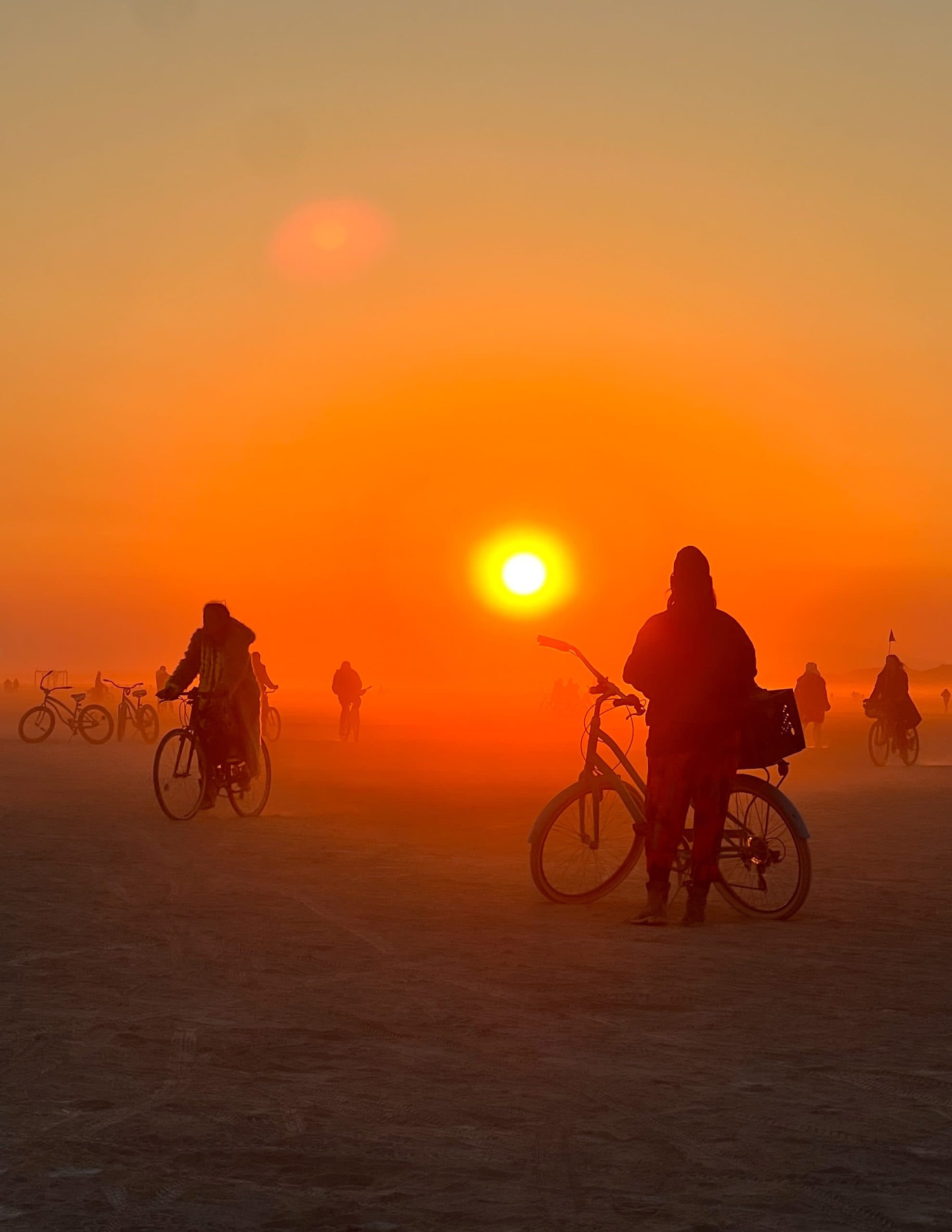 Silhouettes of people biking at Burning Man illuminated by the red and orange light from the sunrise.