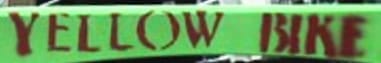 Painted label on green bike frame indicating a Yellow Bike from the Yellow Bike Community Program at Burning Man.