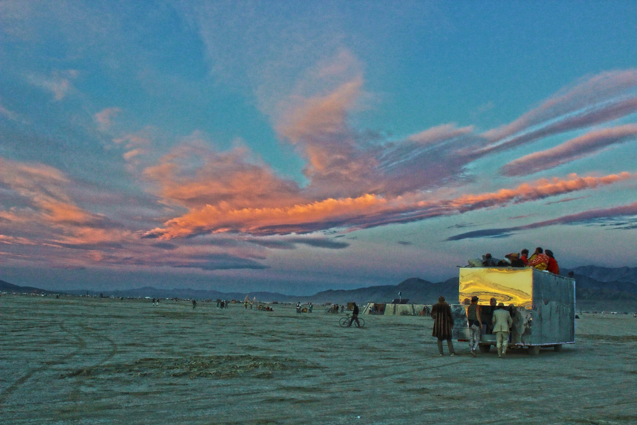 A Burning Man sunset sky showing many vibrant pink clouds with an art car and the mountains in the distance.