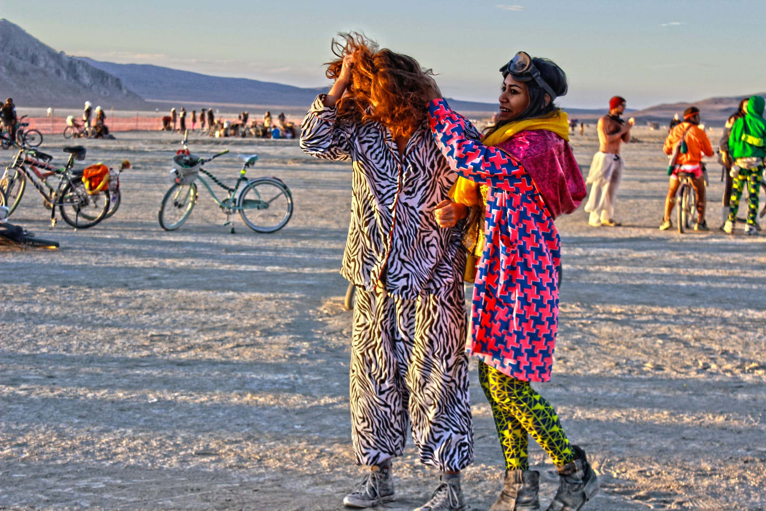 Two people at Burning Man during sunrise wearing very vibrant patterned outfits. The outfits are thick and they look warm.