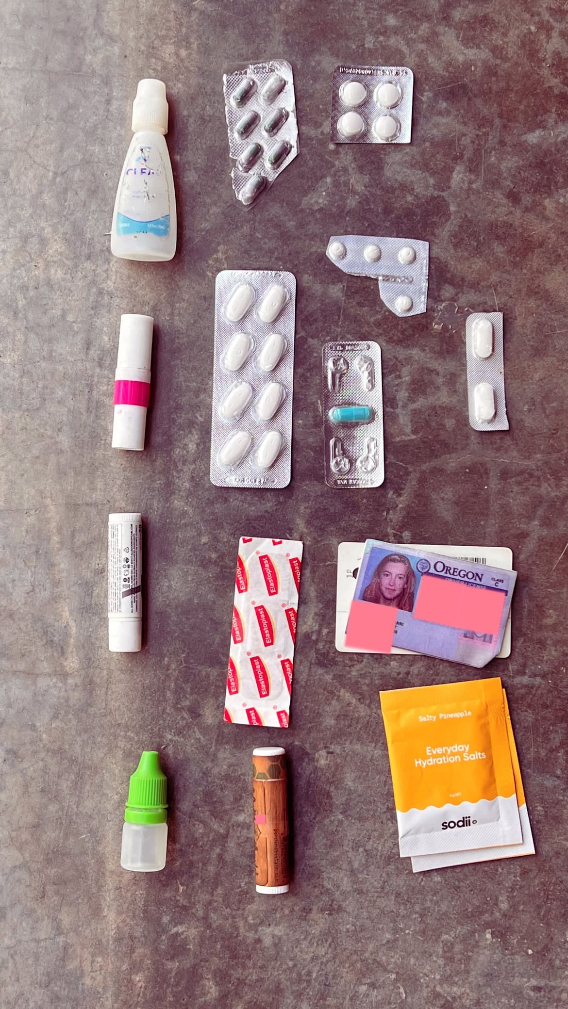 Packing items for festival Burning Man for a go bag laid out on the grounf including ID, chapstick, eye drops, and electrolytes.
