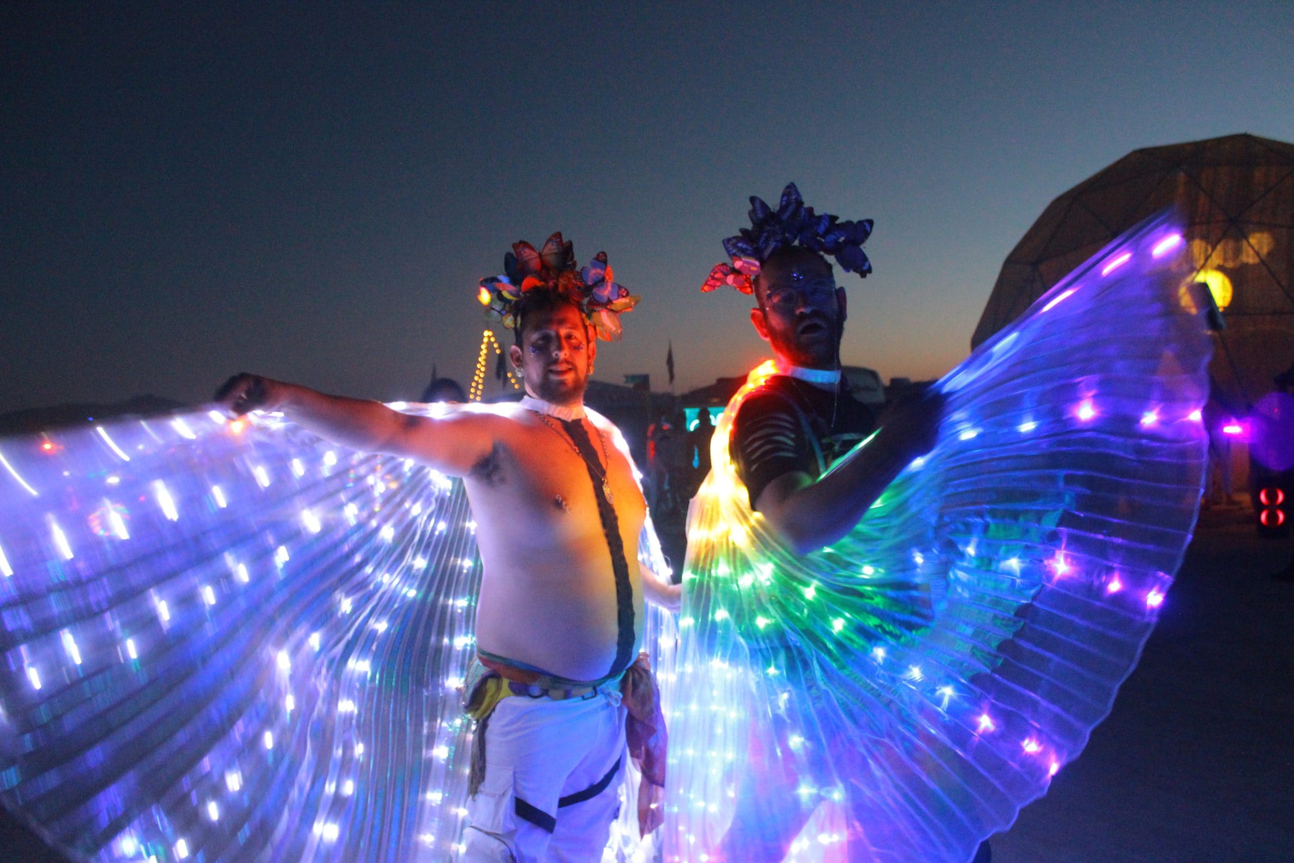 Two friends at Burning Man at night lit up by their vibrant light capes.