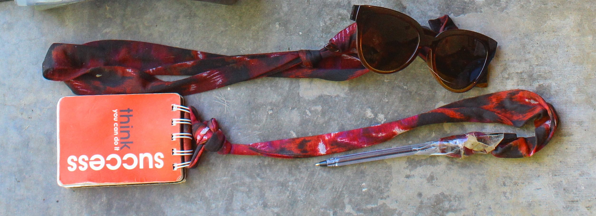 Small journal with a string and pen attached to the binder rings and sunglasses with an attached fabric acting as an eyeglass cord.