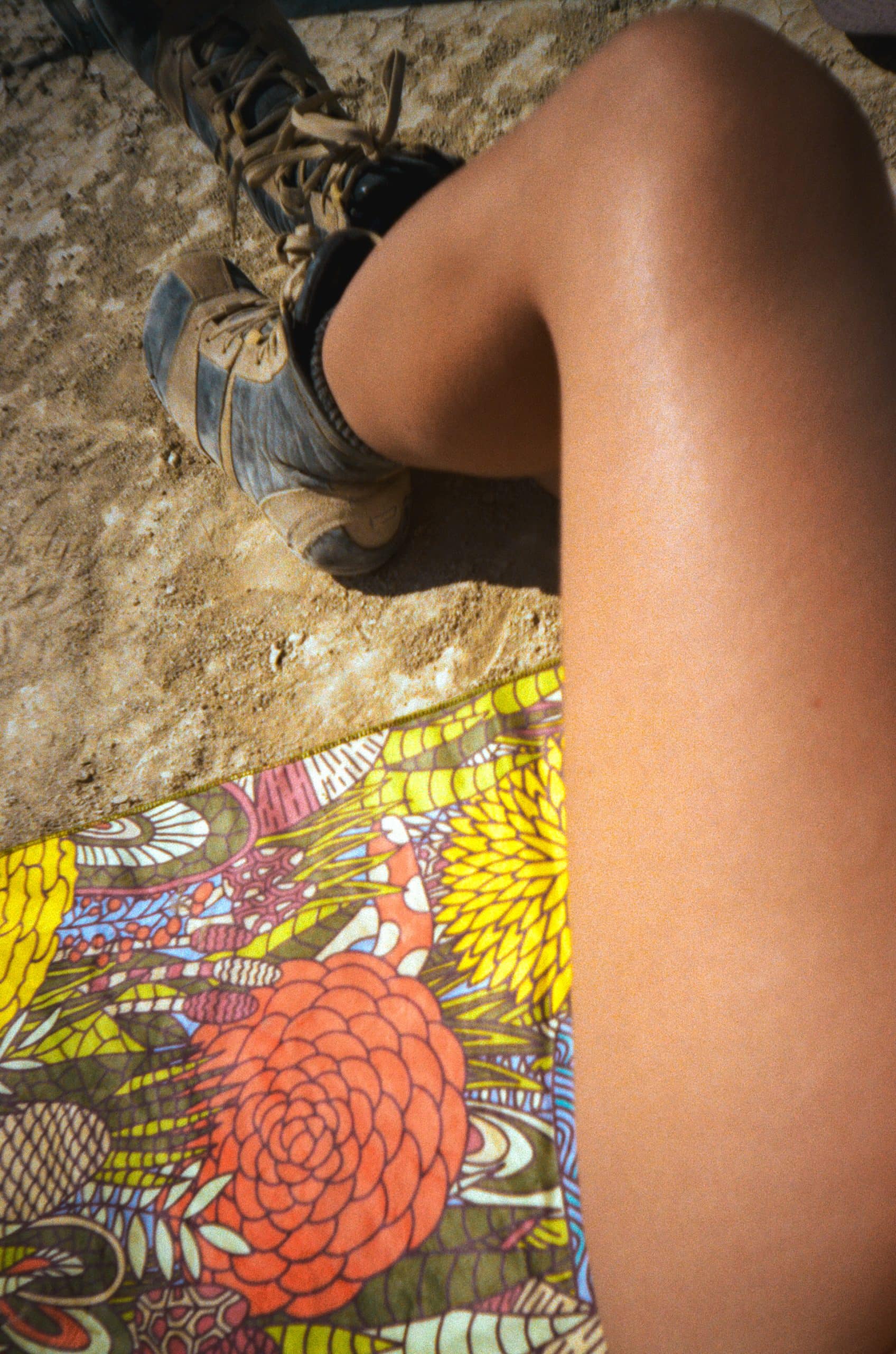 Micro Fiber towel with vibrant design laying on the desert floor at Burning Man. Tan and dusty legs with boots lay on the towel.