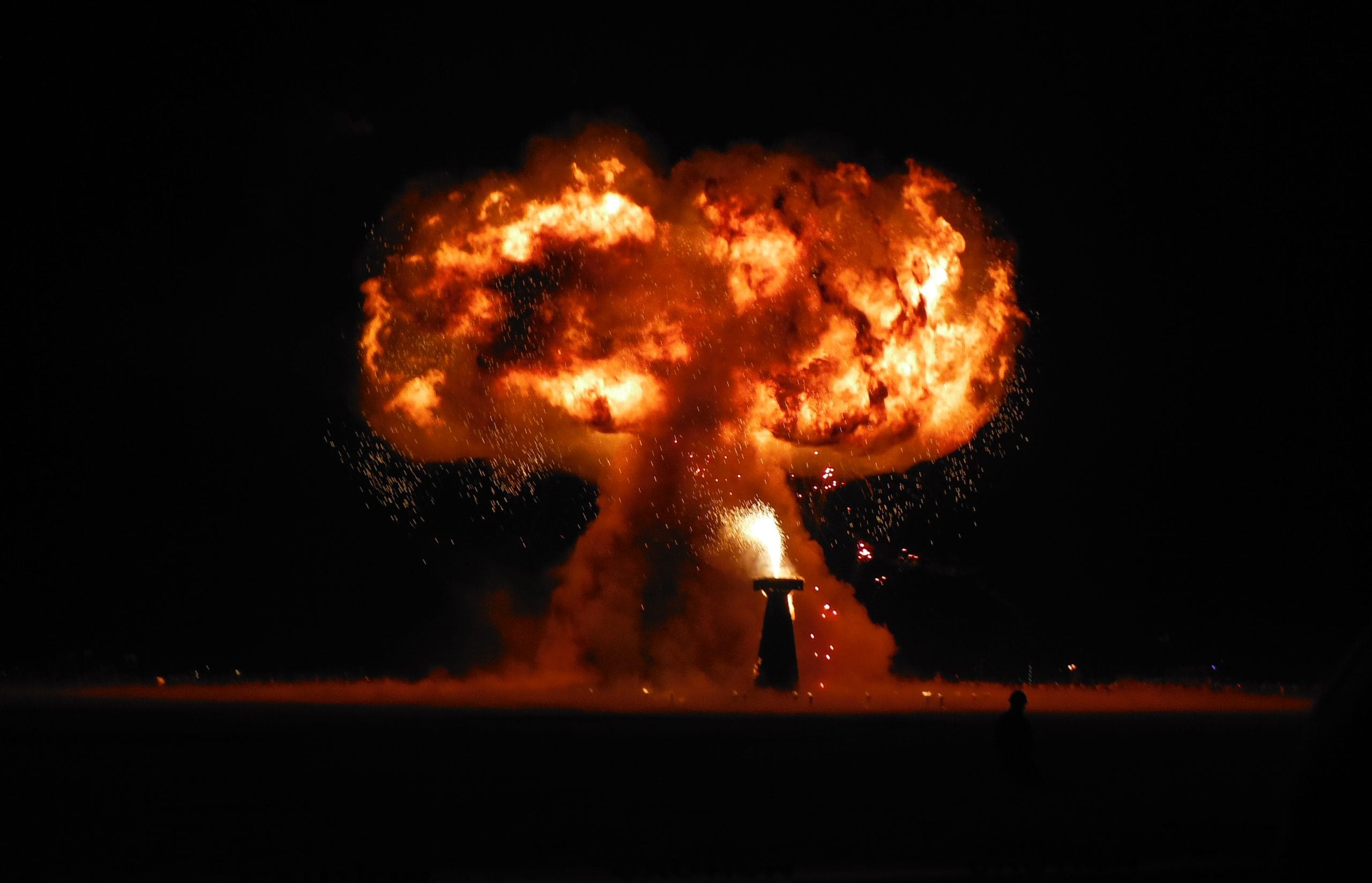 A huge mushroom-shaped fire explosion from an art installation at Burning Man in 2014. The red and orange fire lights up the dark sky.