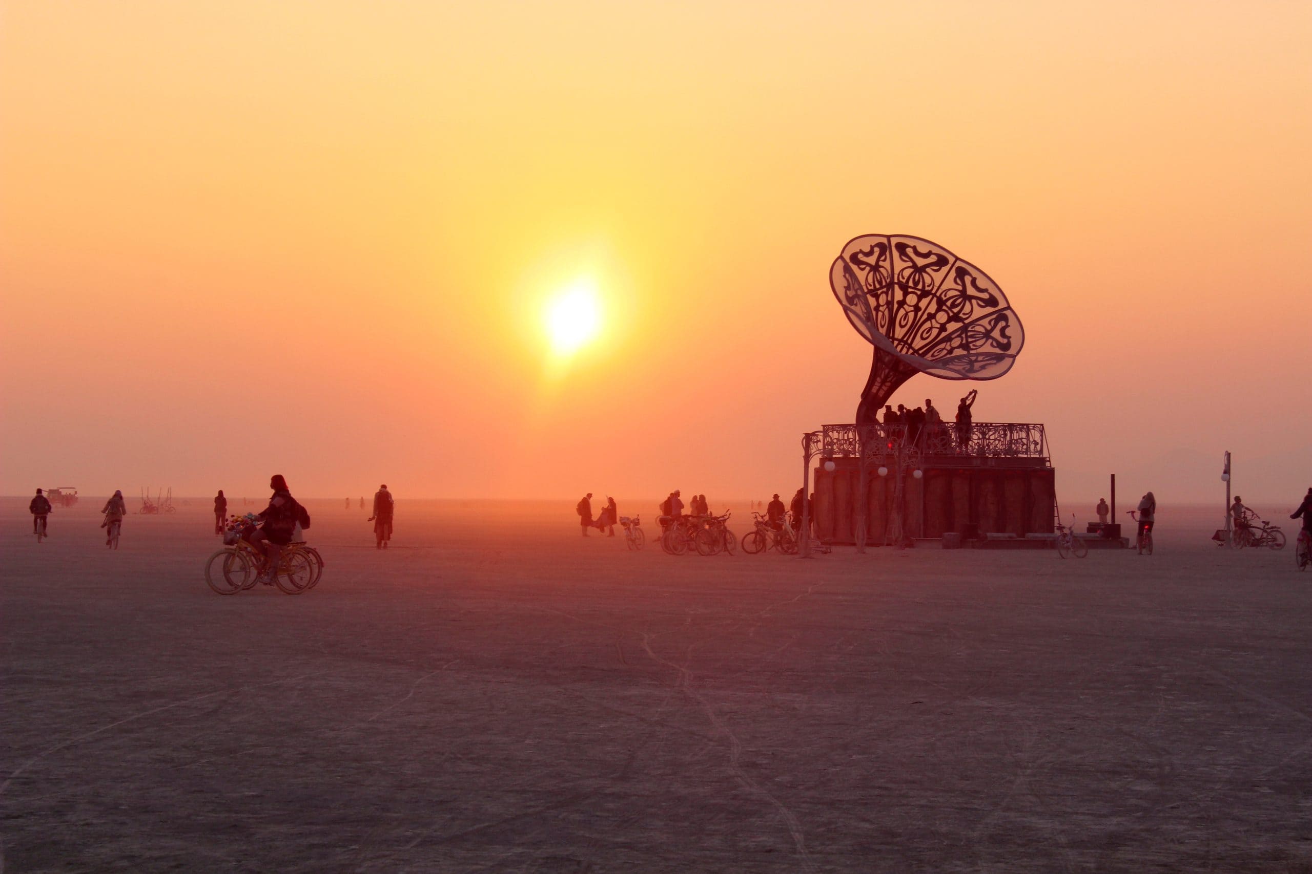 Giant vintage gramophone as an art installation at Burning Man during sunrise with an orange sky.