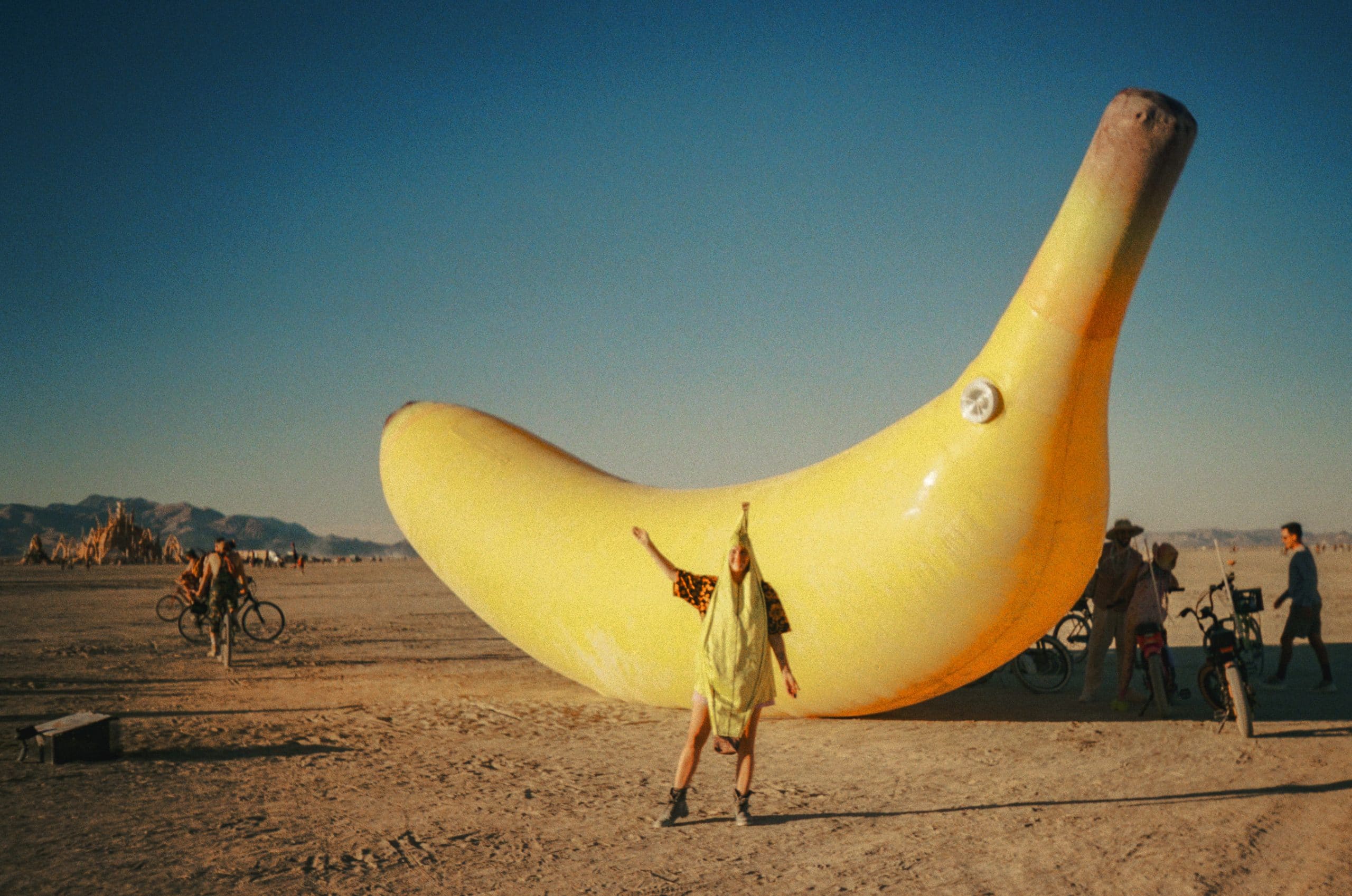 Tasha in a banana costume in front a giant inflatable banana art installation at Burning Man with hills and the temple in the background.