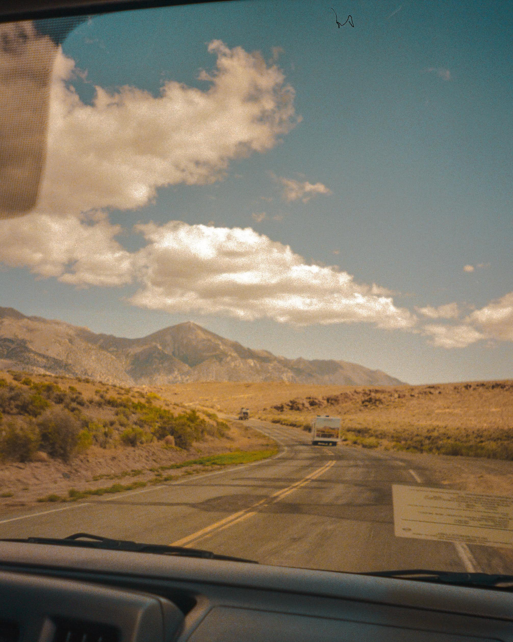 View outside car front windshield showing a road with Uhaul in front and surrounding hills in the Nevada desert, clouds, and blue skies.