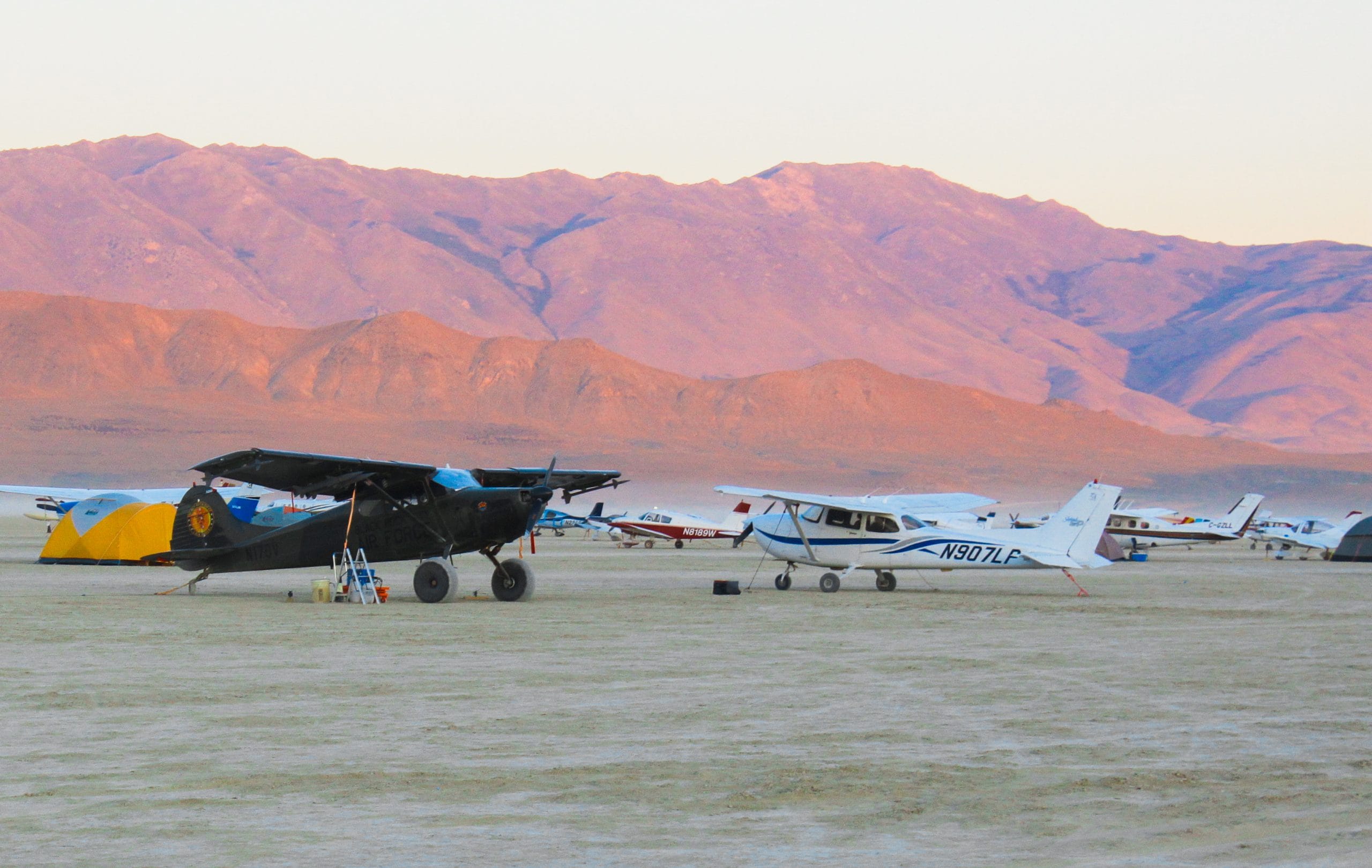 Planes in the desert of Burning Man showing the Black Rock City airport. In the distance there are hills surrounding and they are pink and purple because the sunrise.
