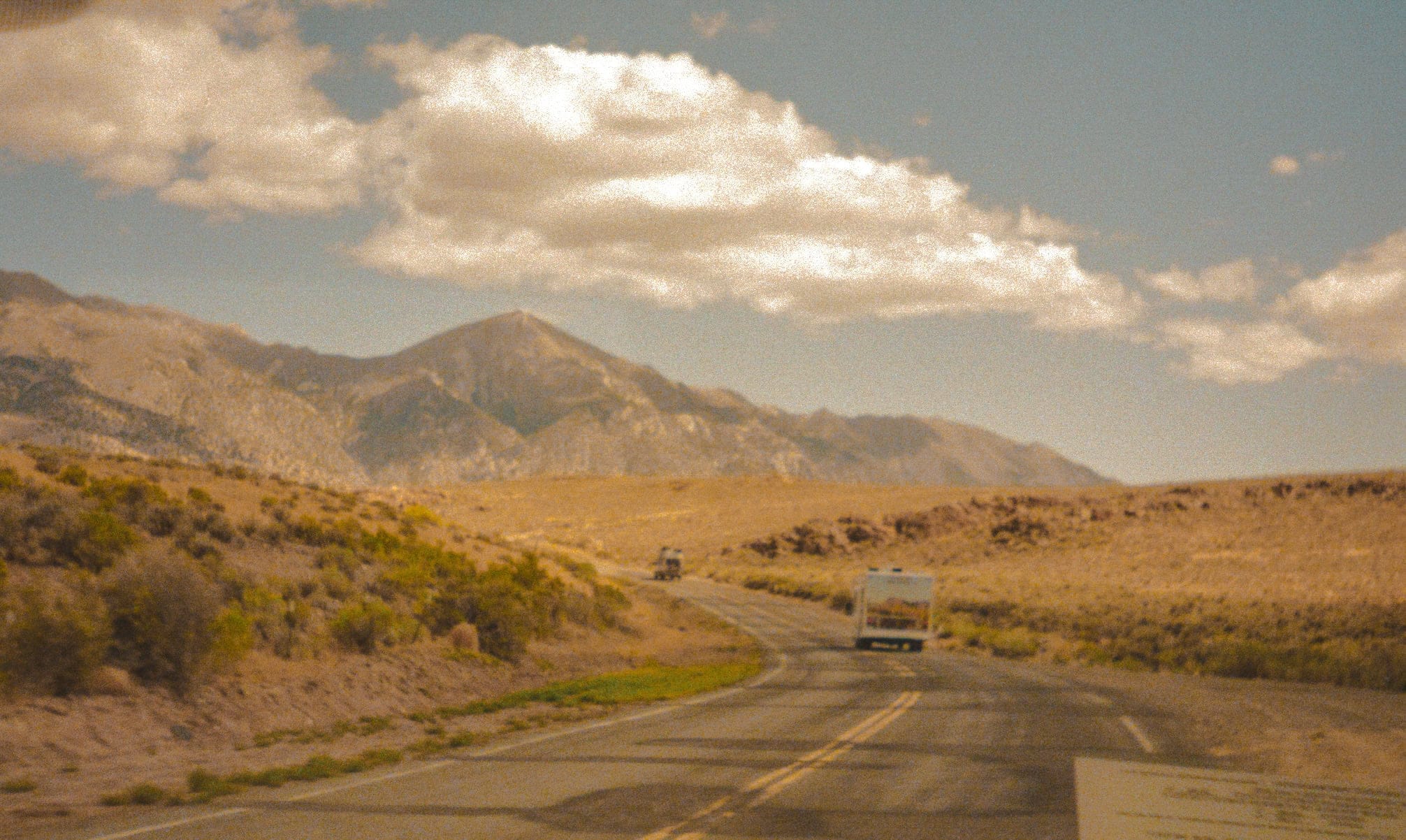 View from the road leading into Burning Man, surrounding hills and dusty ground. A road with a U-haul ahead.
