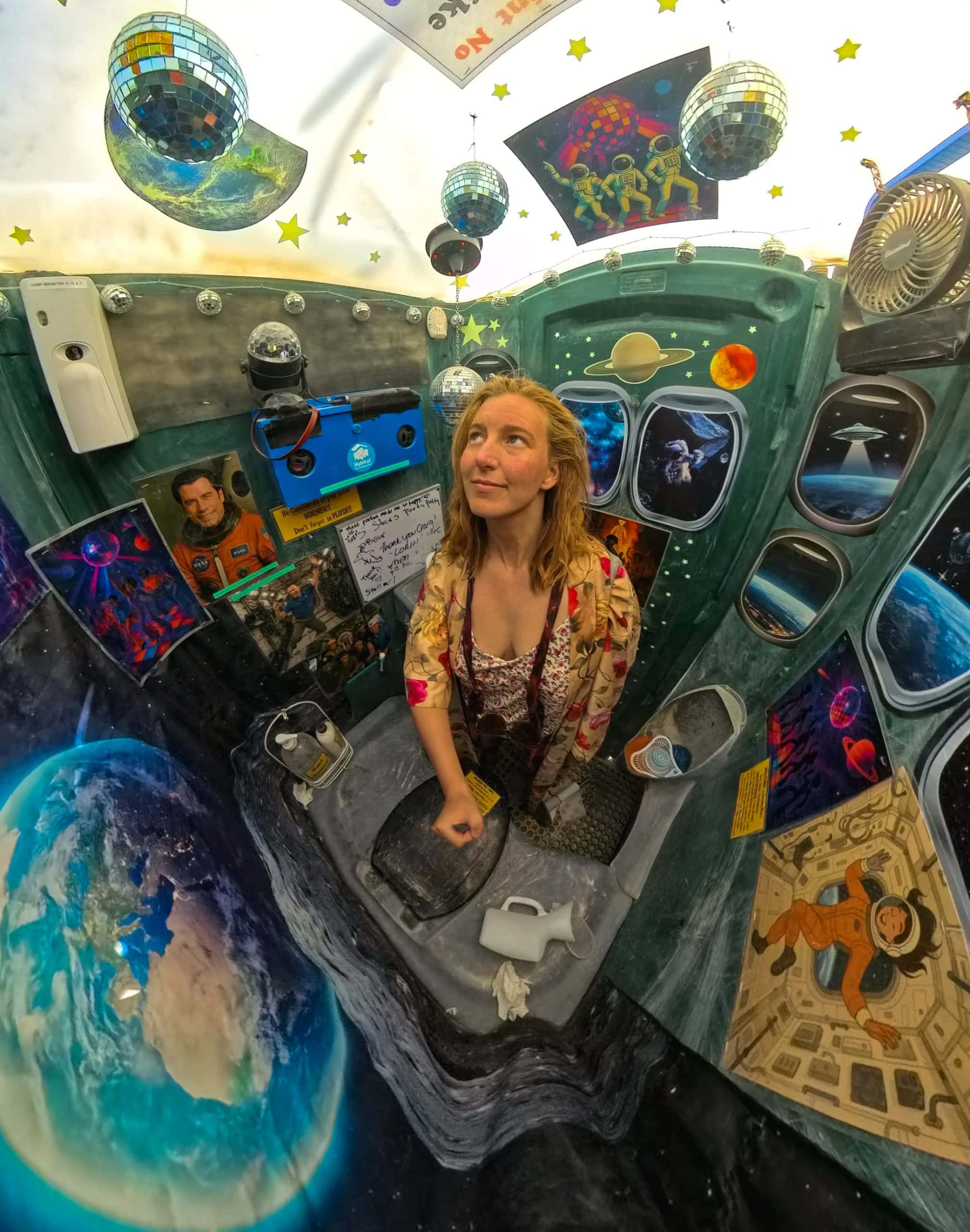 Semi fish eye view of Tasha in a porta-potty at Burning Man taken with an insta360. Inside the porta-potty is decorated like a disco with many disco balls, posters of disco singers, and small jukebox that played disco fever songs.