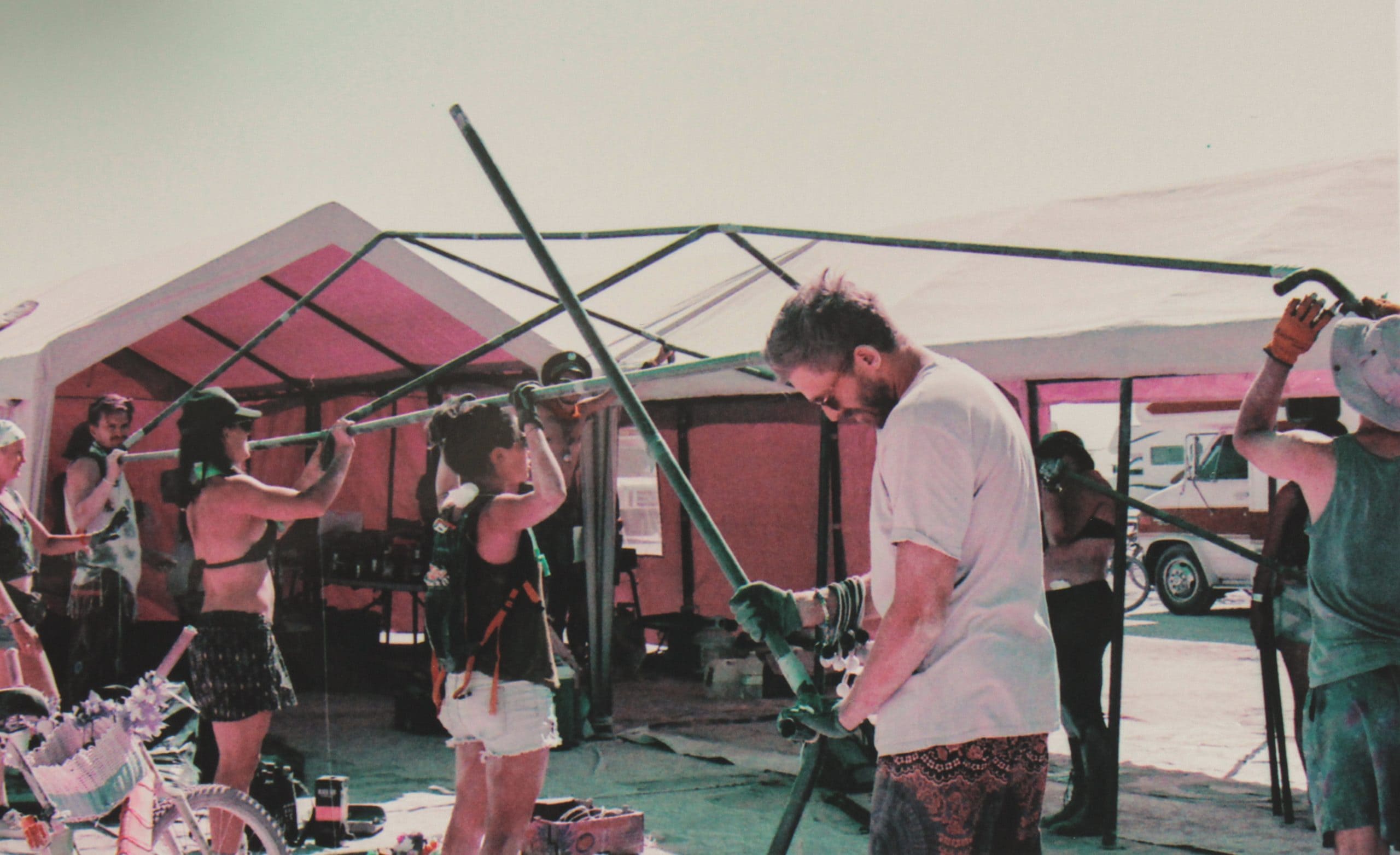 Campmates setting up the poles and cover of a carport structure at Burning man on an overcast day.