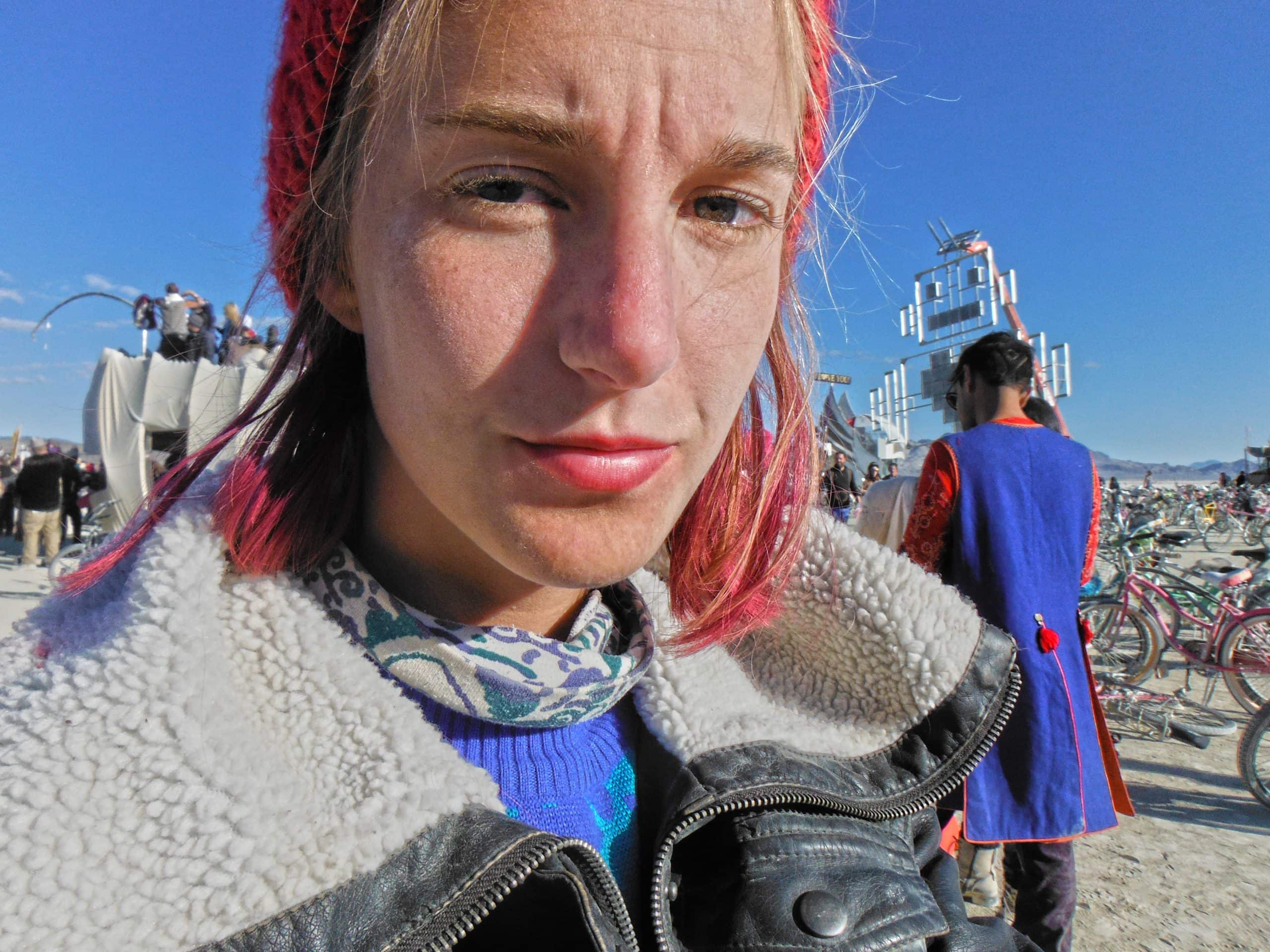 Tasha the blogger looking into the camera looking tan and dusty at sunrise at Burning Man by the Robot Heart art car.