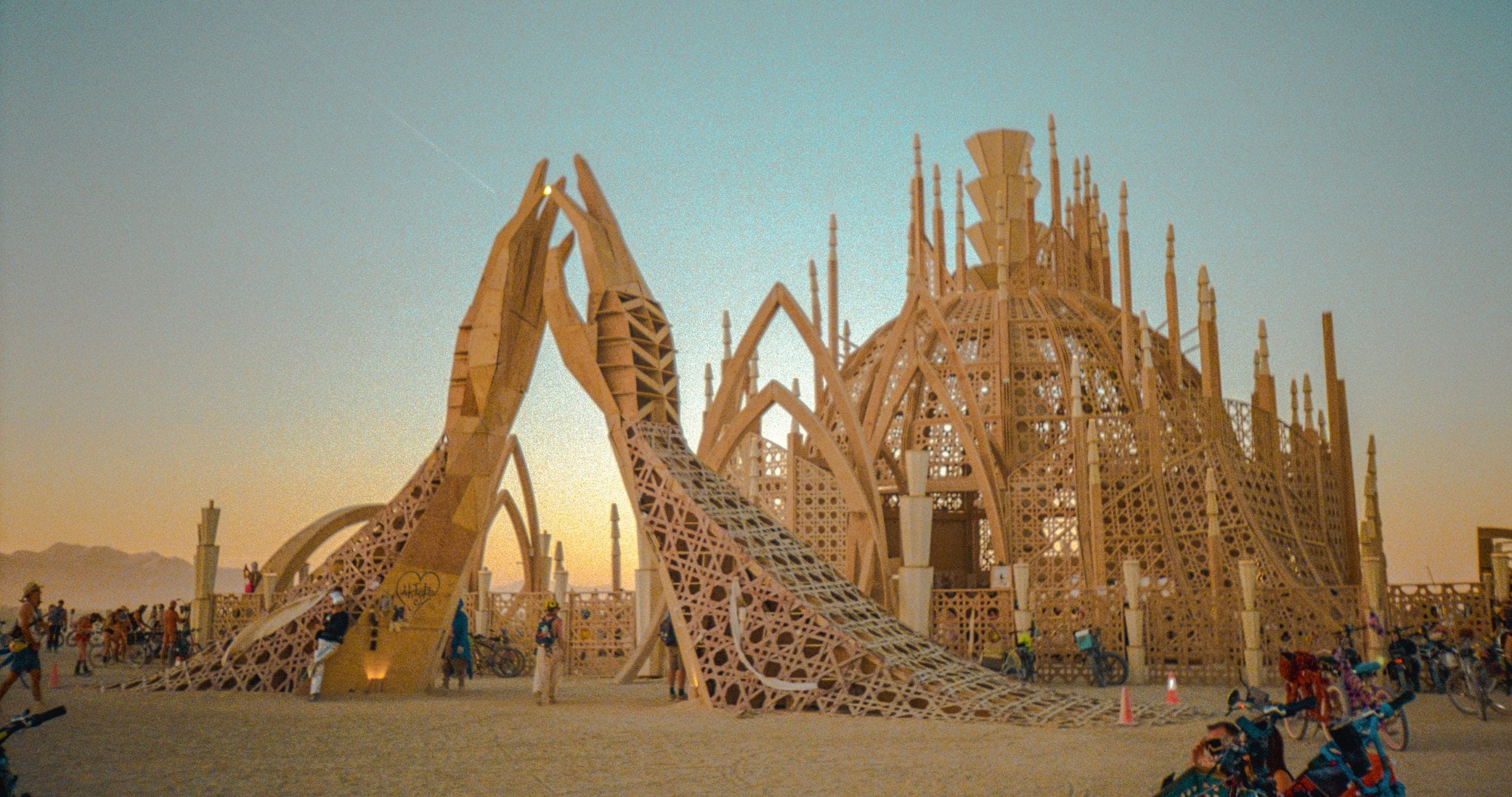 Wooden temple structure at Burning Man called Temple of Together. Wooden beams form two hands that look like praying towards the sky in front of the main part of the structure.