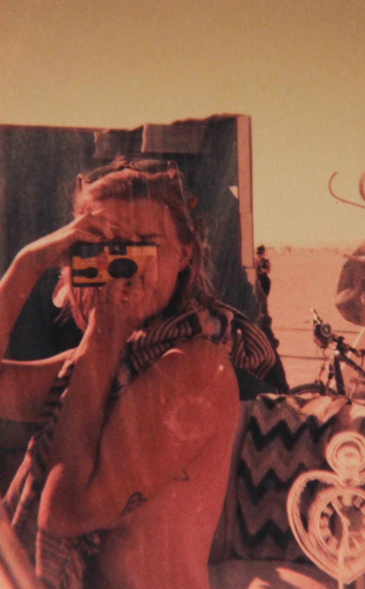 Tasha taking a selfie with a disposable camera in a mirror in a house art installation at Burning Man.
