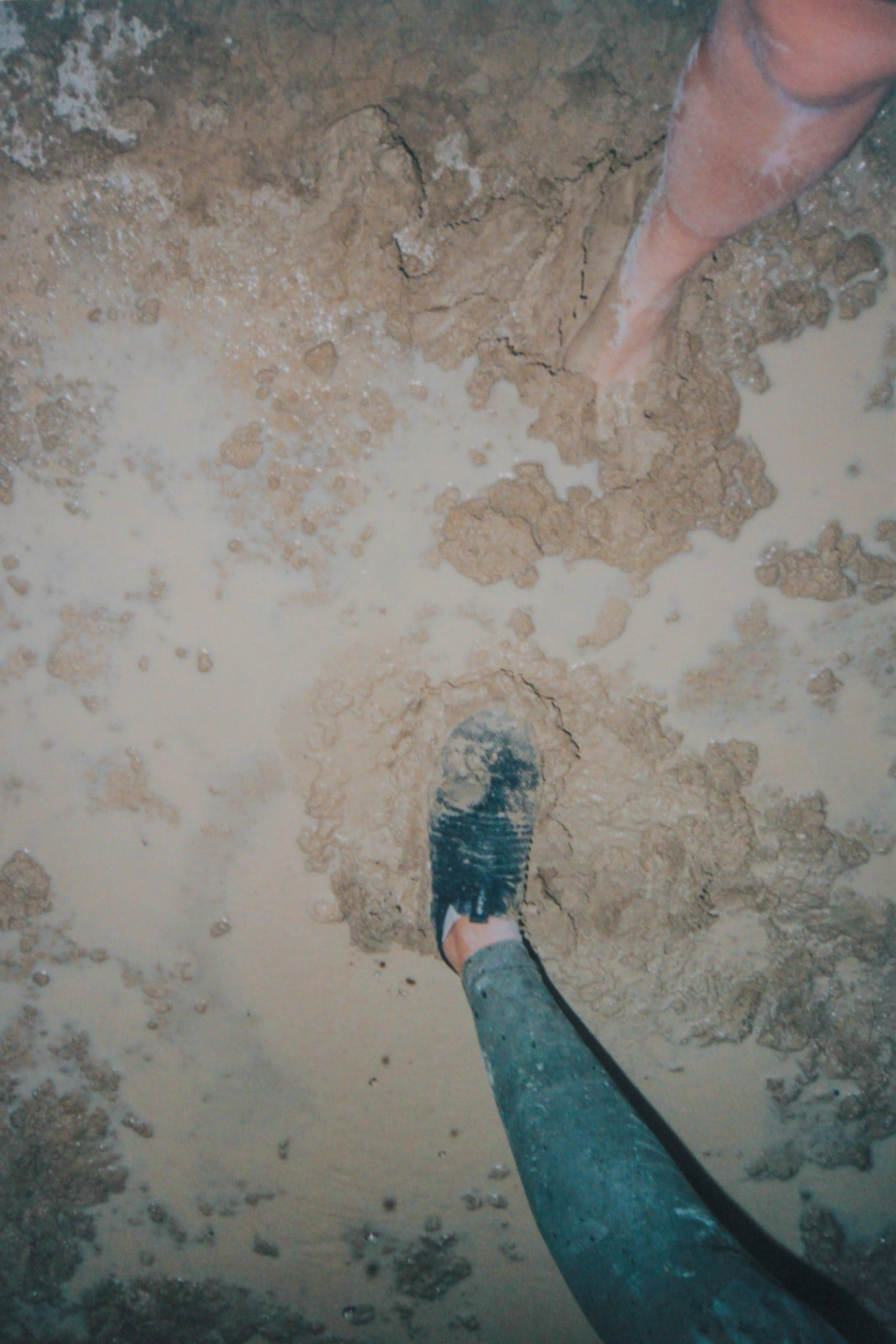 Two legs of different people in the wet playa mud at Burning Man showing the deep holes after it rains making the roads bumpy.