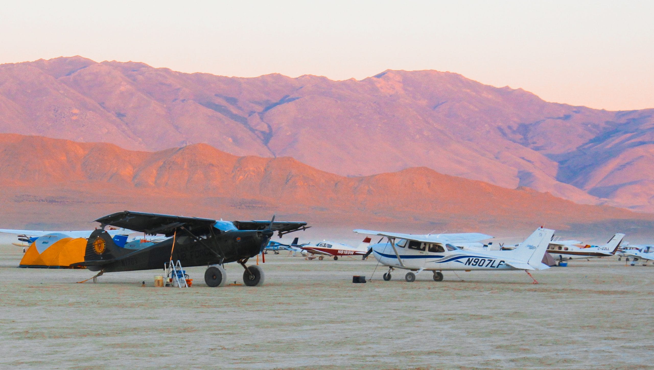 Airplanes at sunrise on the dusty ground at Burning Man during a volunteer shift working GP&E. Mountain hills in the distance covered in pink and orange light from the sun rising.