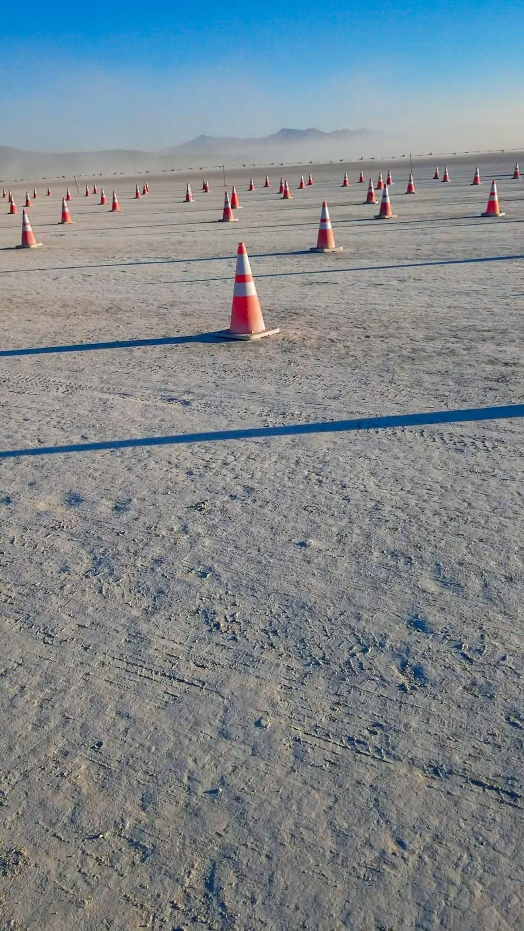 The driving lanes at the entrance Gate at Burning Man but with no cars, just traffic cones separating the lanes in straight lines. Small dust storm in the far distance and blue skies.