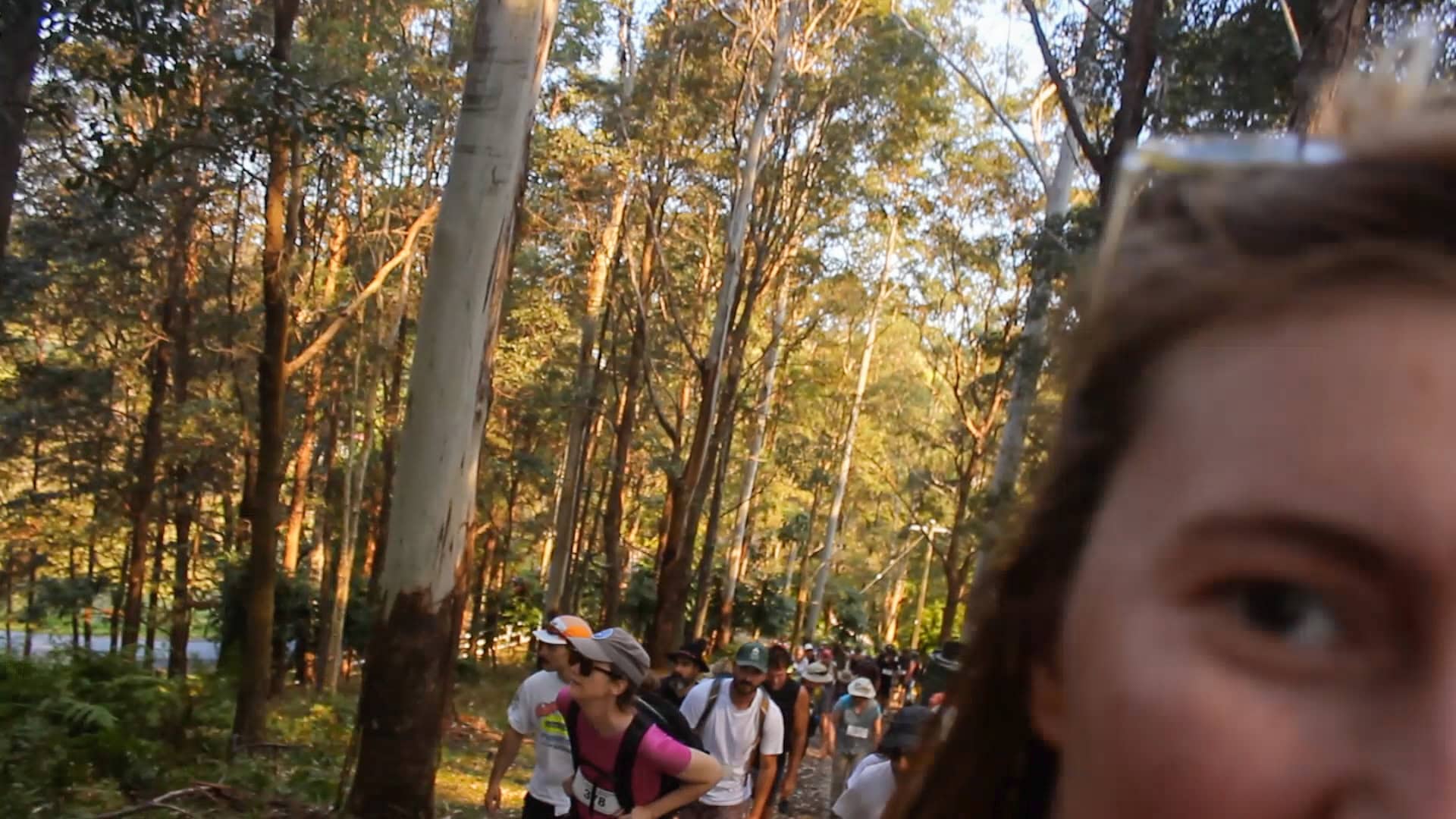 Tasha on the right looking into the camera and behind her a line of people walking up Mount Chincogan in the tress.