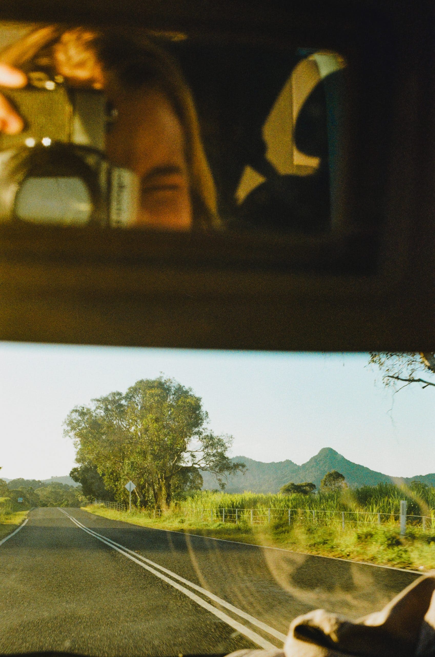 Tasha taking a photo in a car rear view mirror on the top half and below her is the view out of the car windshield of Mount Chincogan and the road leading nearby.
